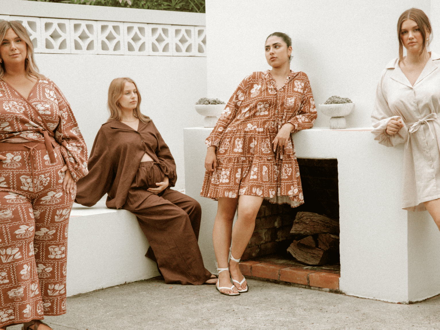 Four women in a backyard area styled in a netural clothing collection in unison, posing and modelling