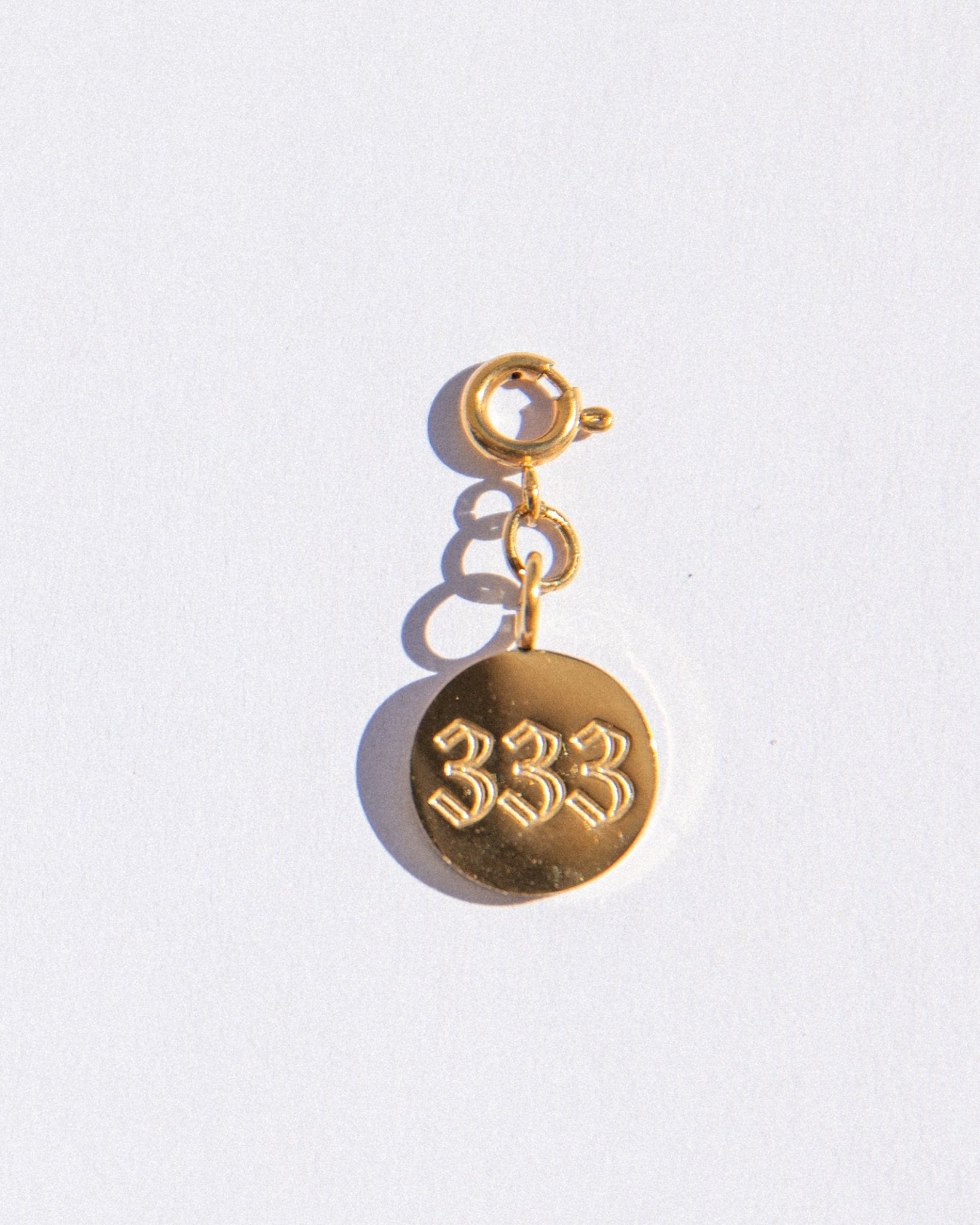 Gold circle charm with angel numbers '333' on a white background