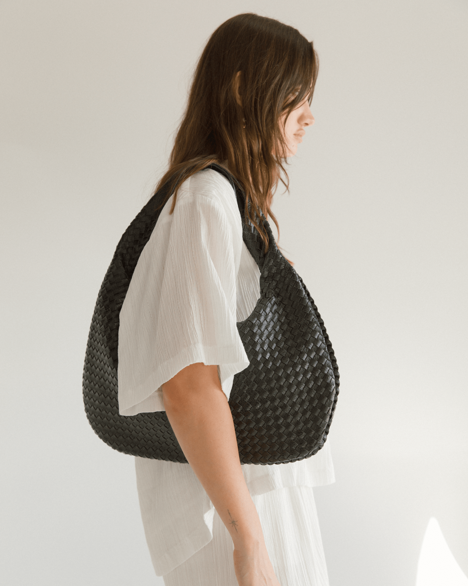 Person wearing a woven black handbag on a plain background