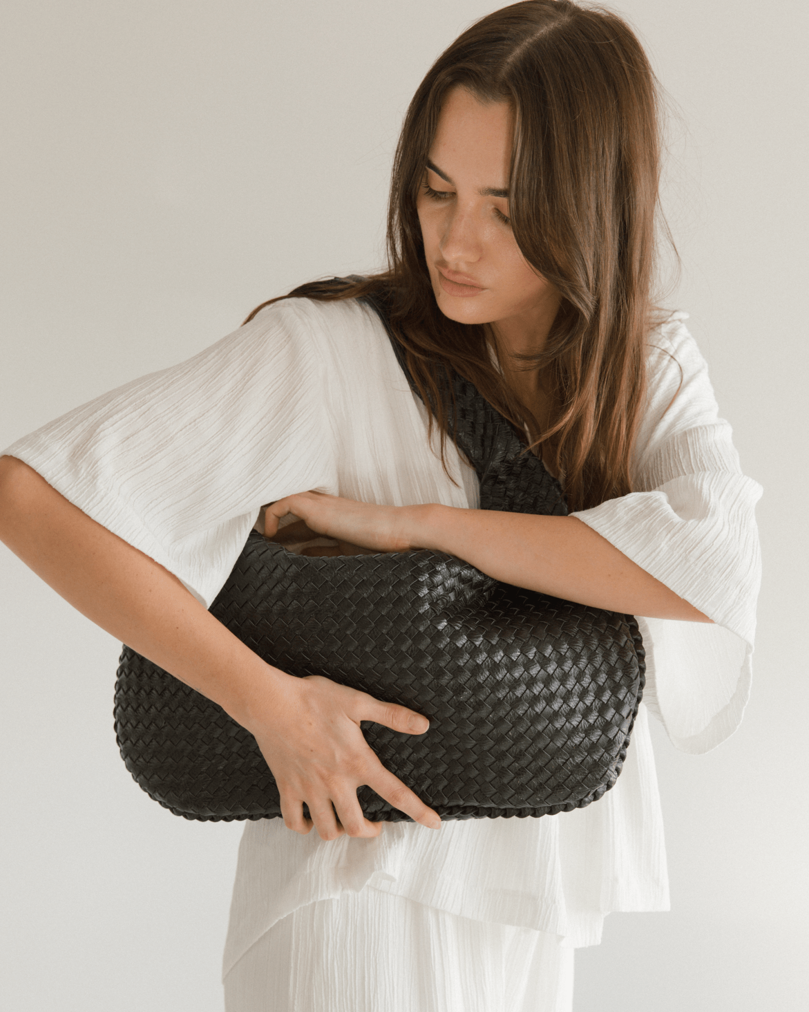 Woman holding a woven black handbag against a plain background