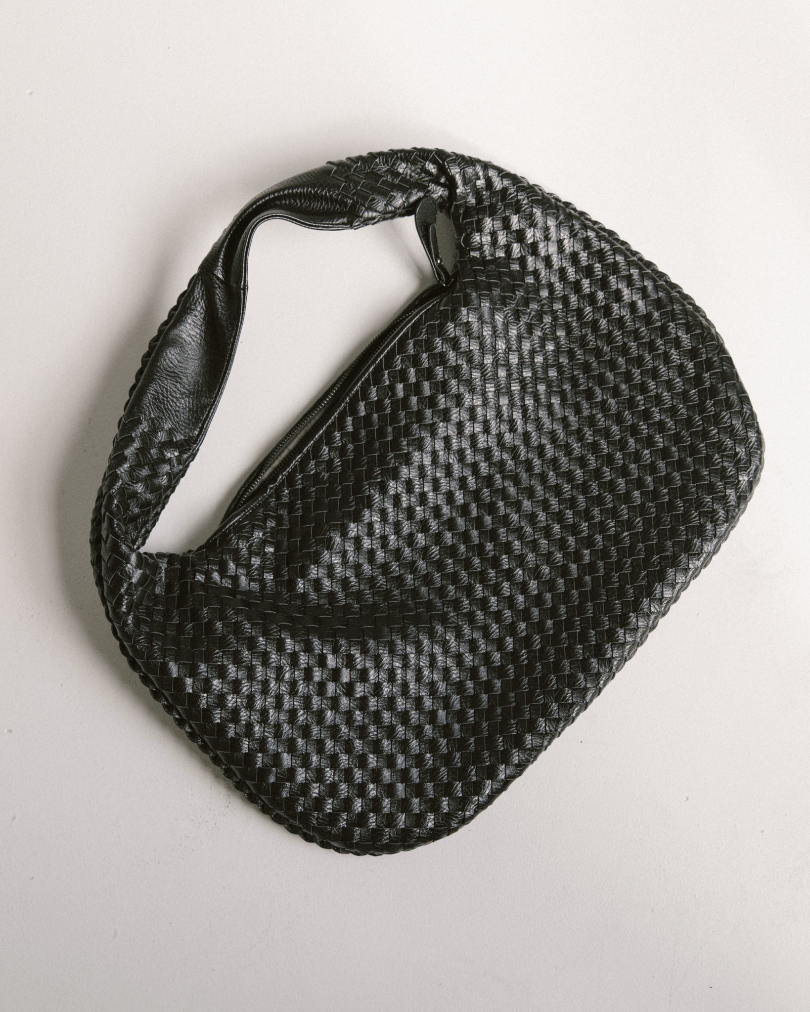 Black woven bag with a strap on a light gray background