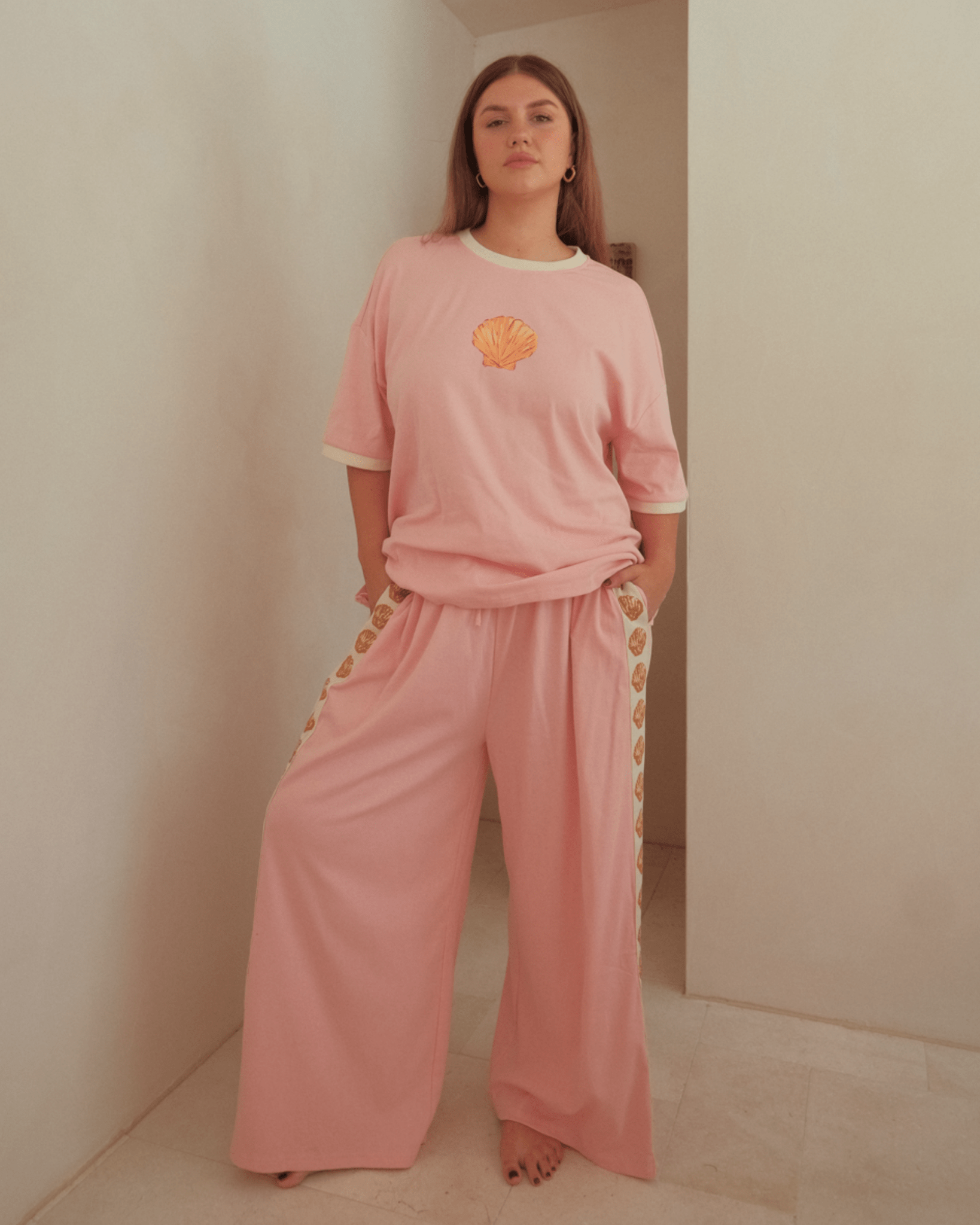 Woman wearing a light pink matching loungewear set with a oversized shirt and wide legged pants.