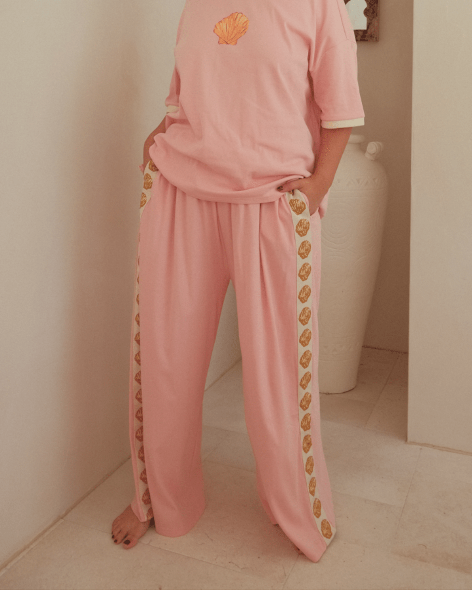 Woman wearing pink a loungewear set with gold shells.