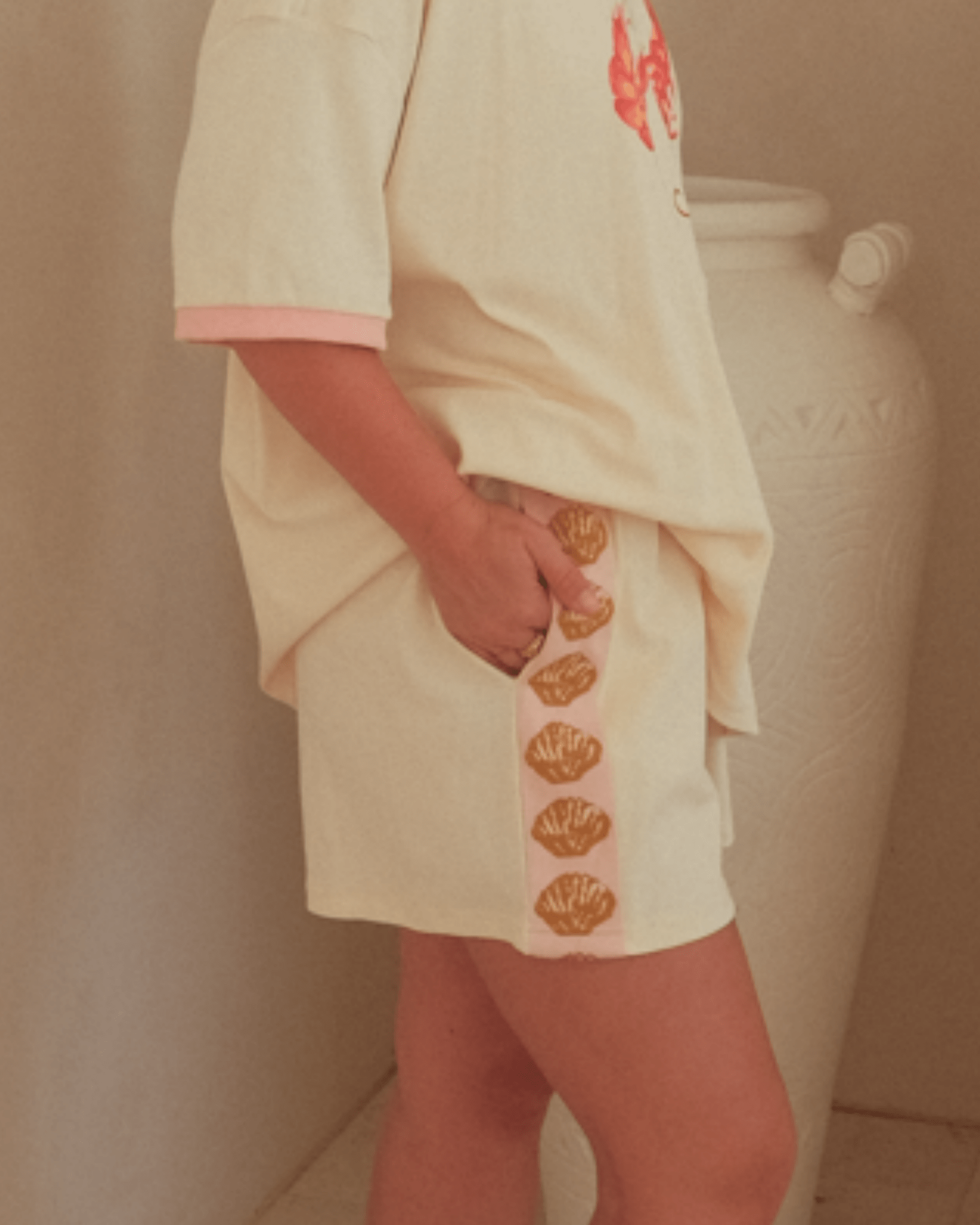Person wearing a cream-colored matching outfit with gold shell detail on shorts.