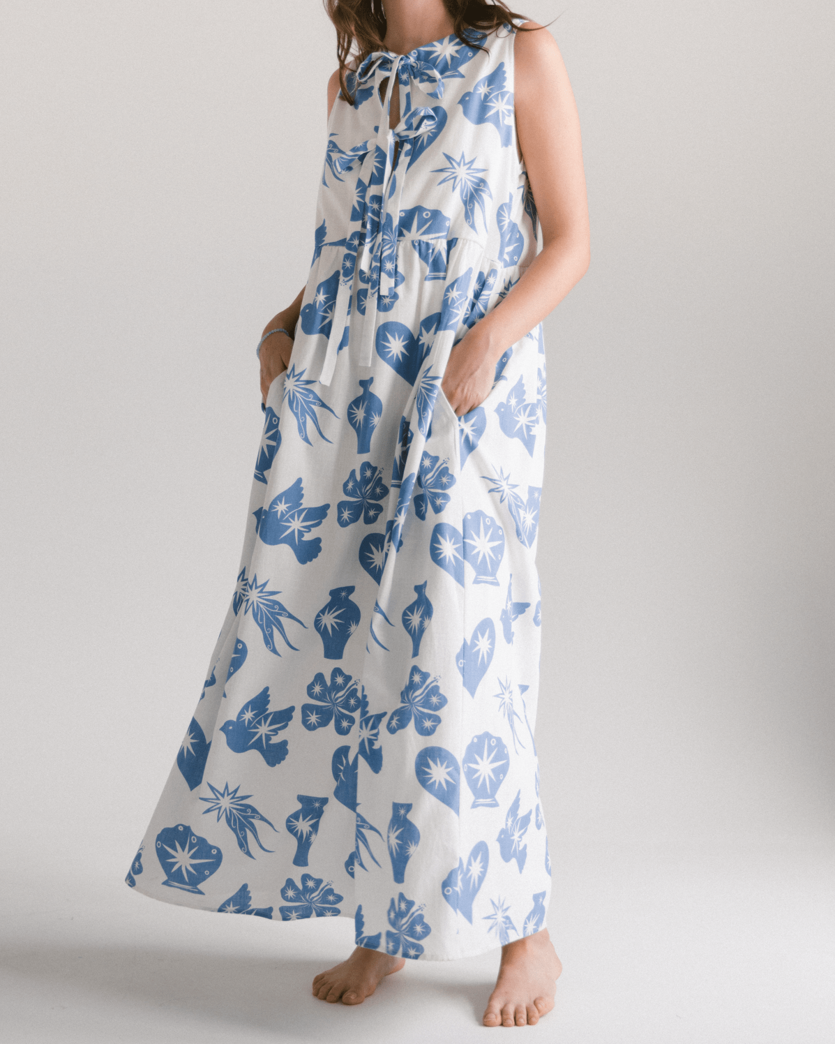 Woman wearing a long dress with blue floral pattern on a plain background