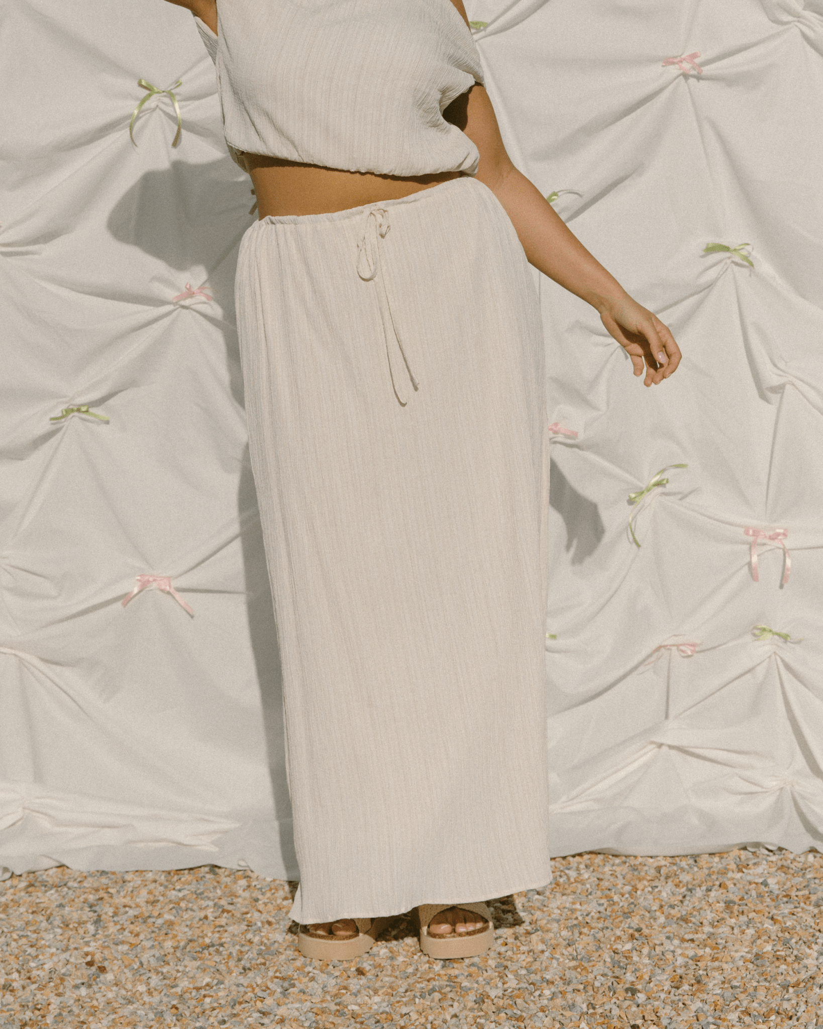 Woman wearing maxi length cream coloured skirt with drawstring waist.
