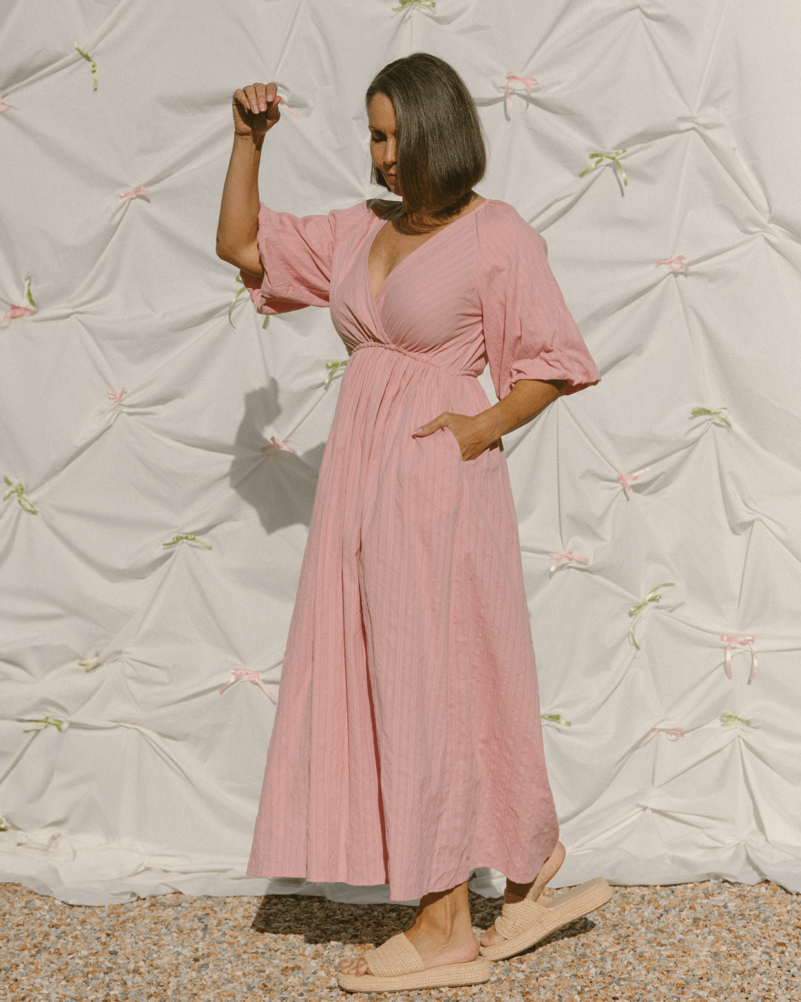 Woman wearing adjustable, breastfeeding friendly wrap dress with pockets in a blush pink colour.