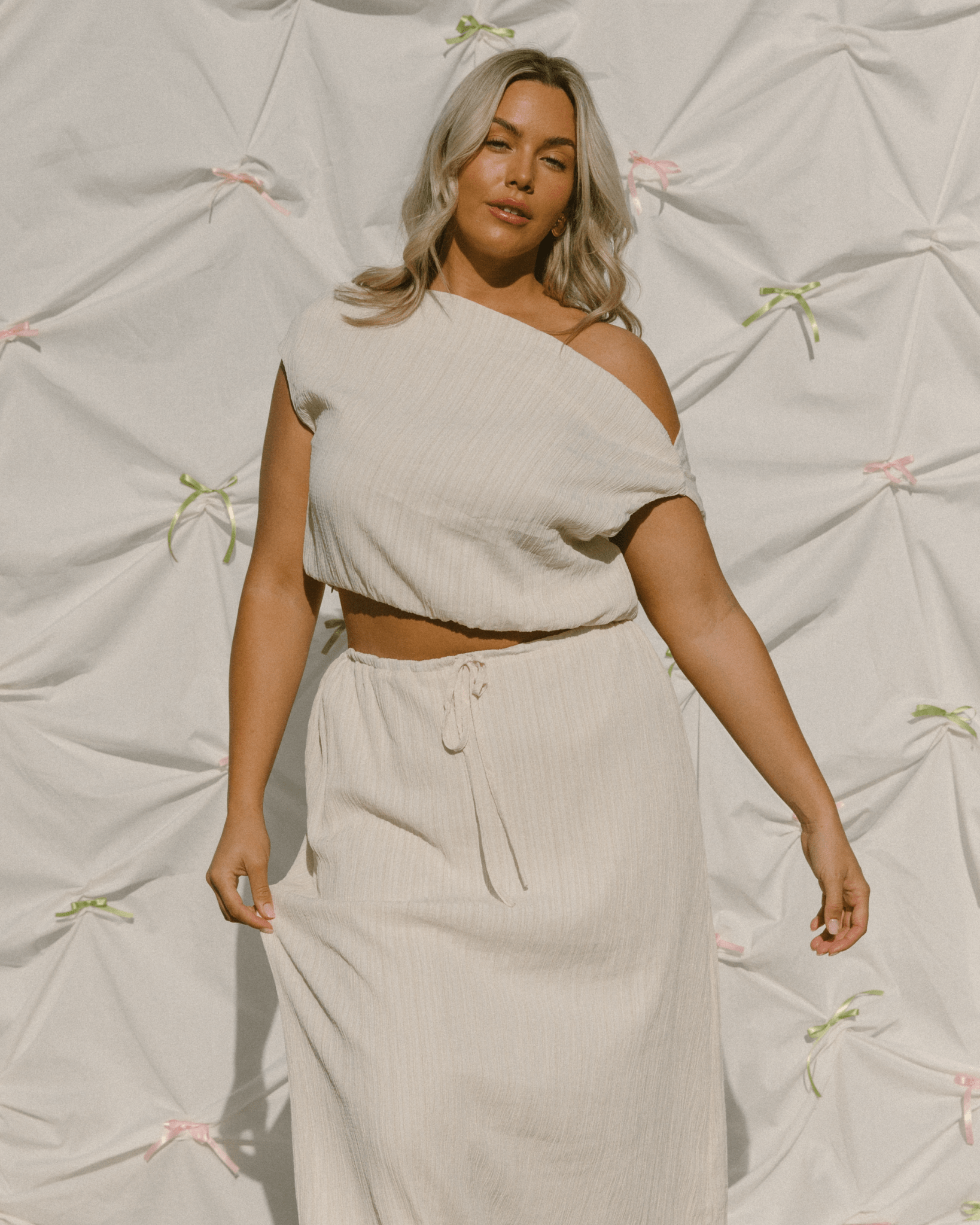 Woman wearing off the shoulder cream crop top and matching skirt.