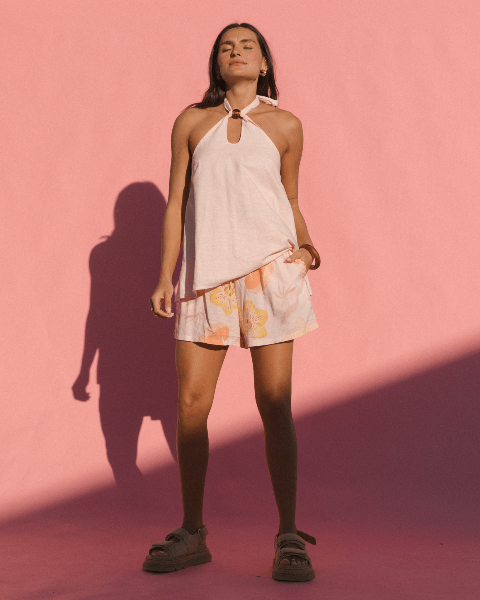 Woman wearing flowy adjustable light pink halter neck top with wide, breathable light pink floral shorts.