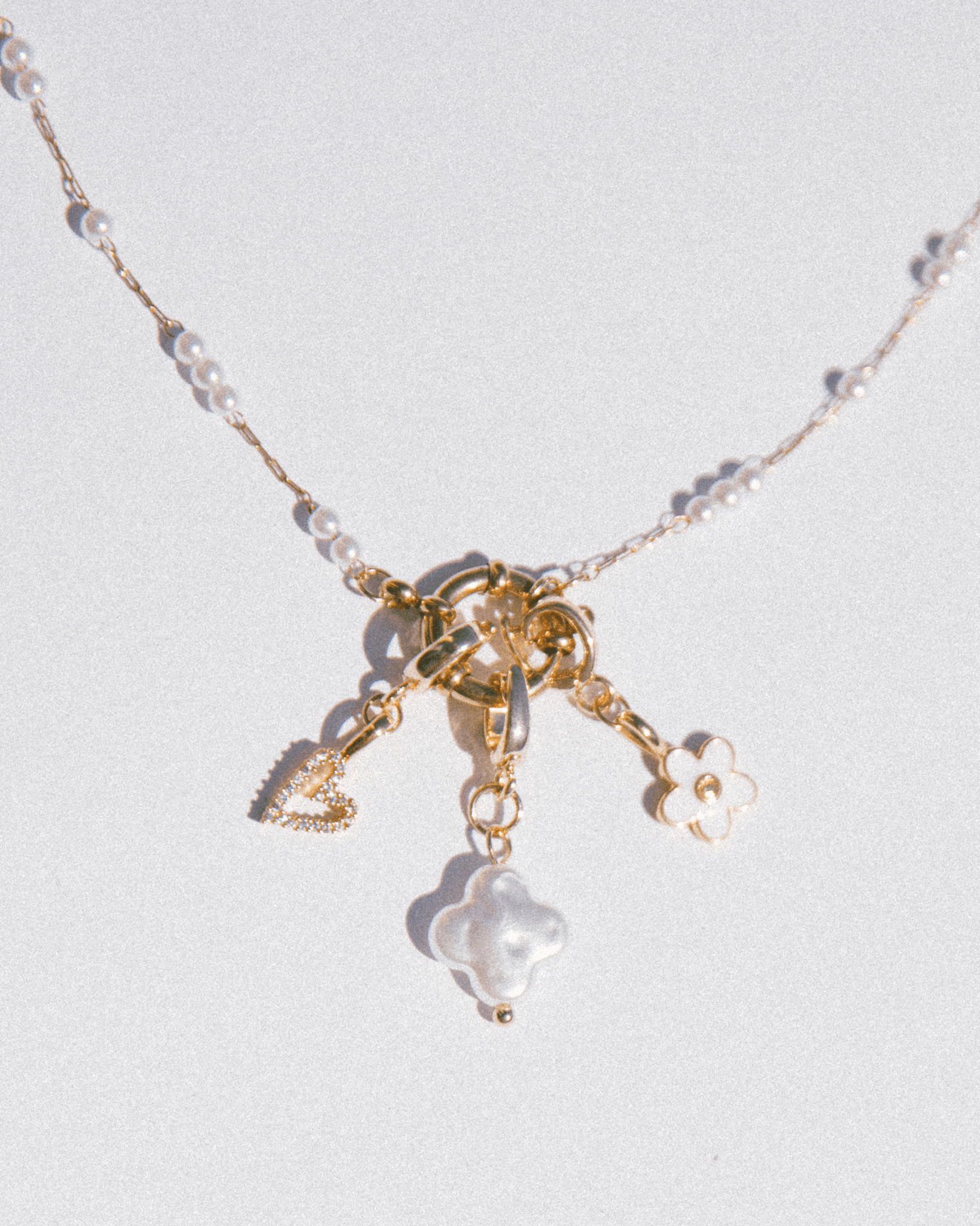 Necklace with gold charms and pearl-like beads on a light gray background