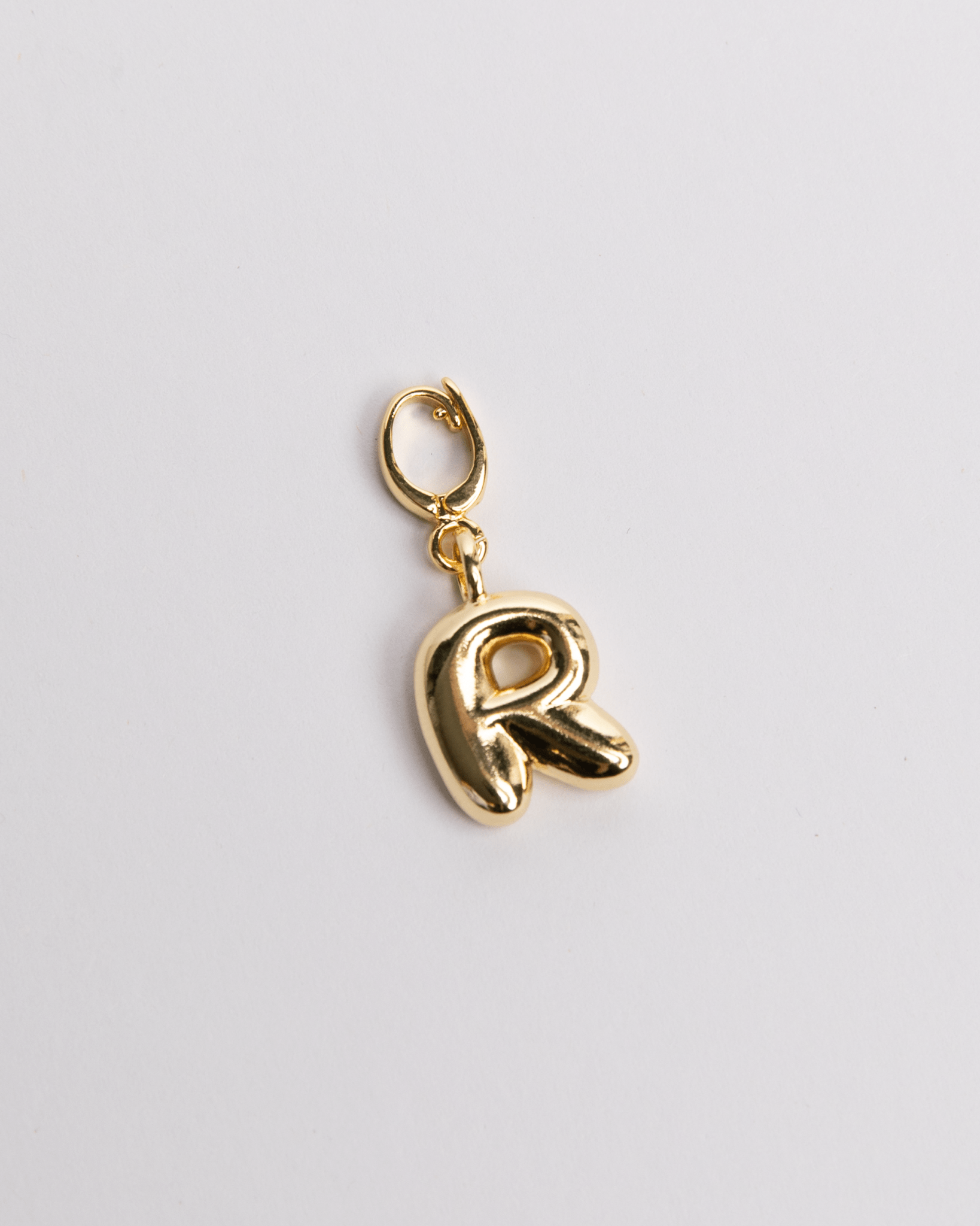 A gold-colored charm in the shape of the letter R with a secure clasp designed for attaching to necklaces or bracelets.