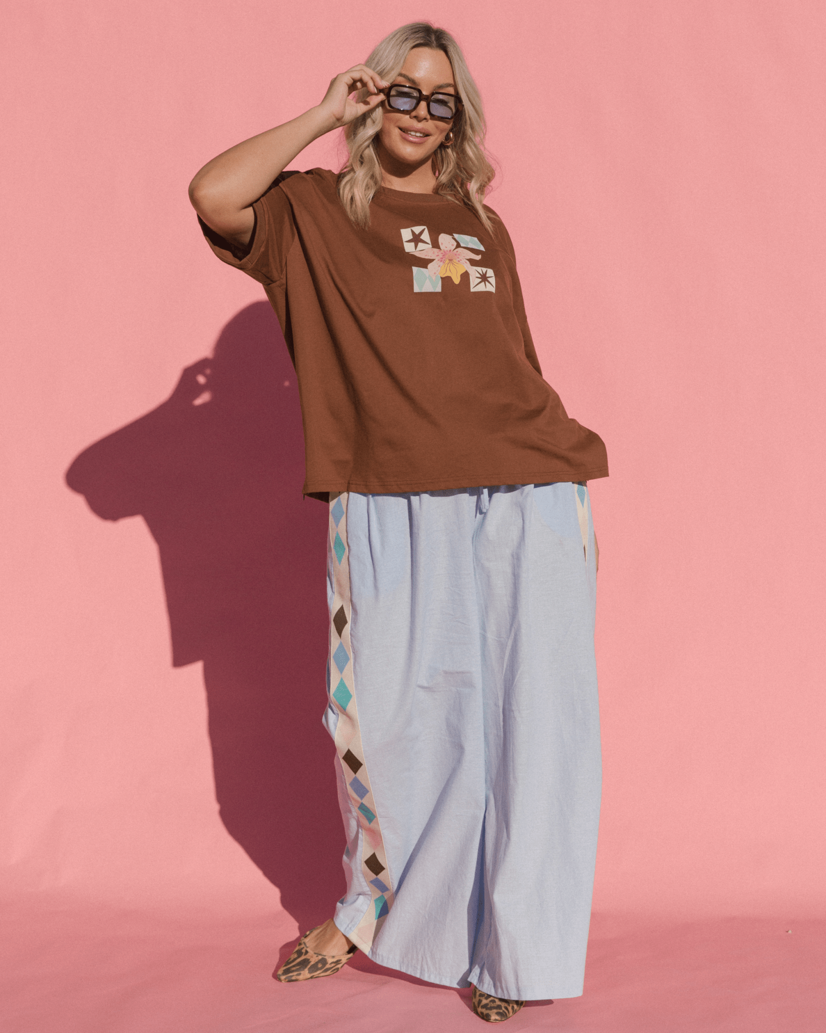 Woman wearing stylish transeasonal outfit with brown graphic tee and light blue pants with diamond pattern down the side.