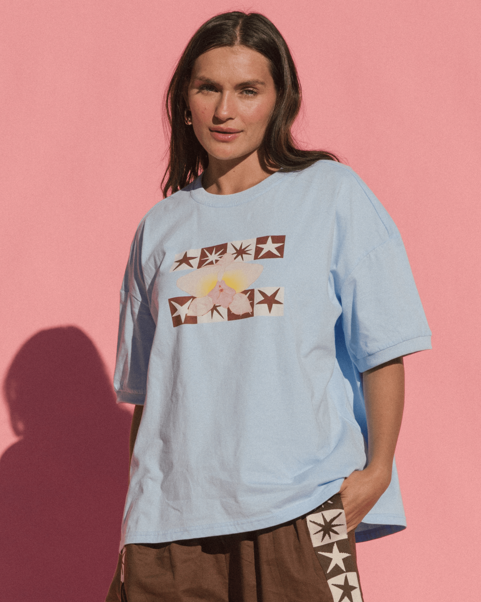 Person wearing a light blue t-shirt with graphic design against a pink background