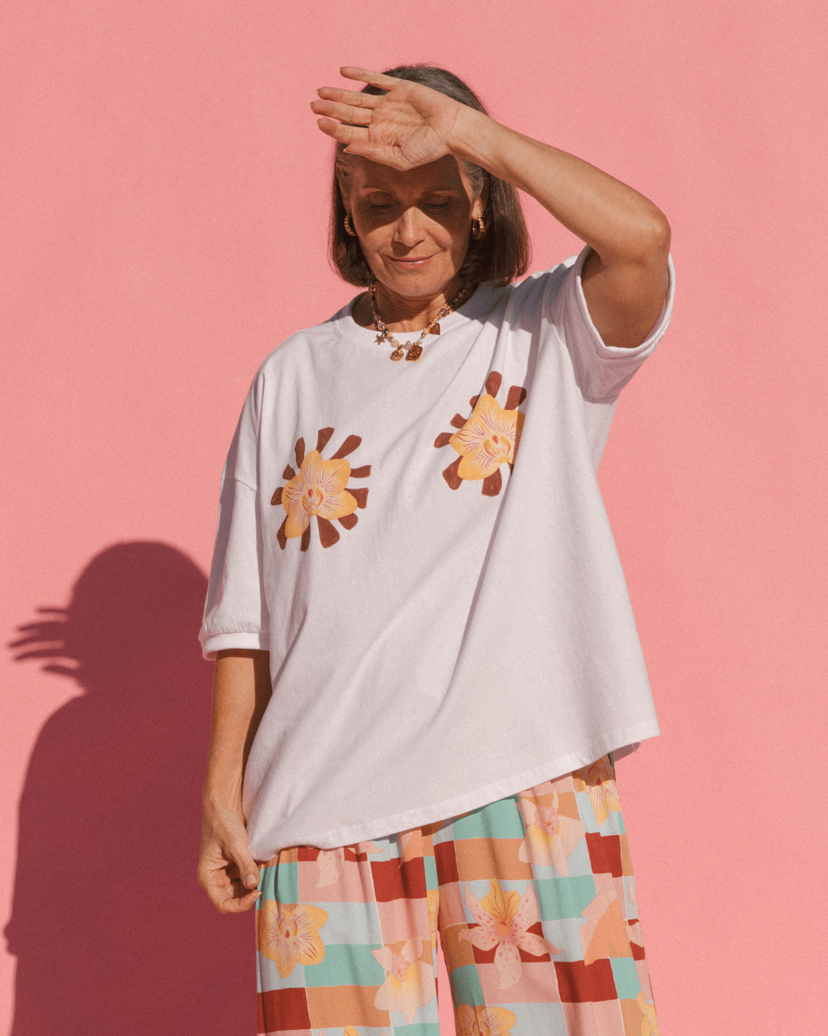 Woman wearing white oversized tshirt with two orchid flower design on the front and geometric floral pants.
