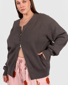 Woman wearing a dark gray cardigan over a pink floral pants on a white background