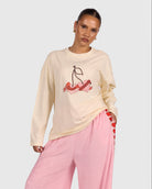 Woman wearing a cream sweatshirt with cherry design and pink pants on a white background