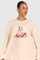 Woman wearing a beige sweatshirt with a cherry design on a plain background