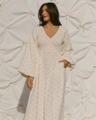 Woman wearing feminine long-sleeved dress with delicate cream and pink flower print. 