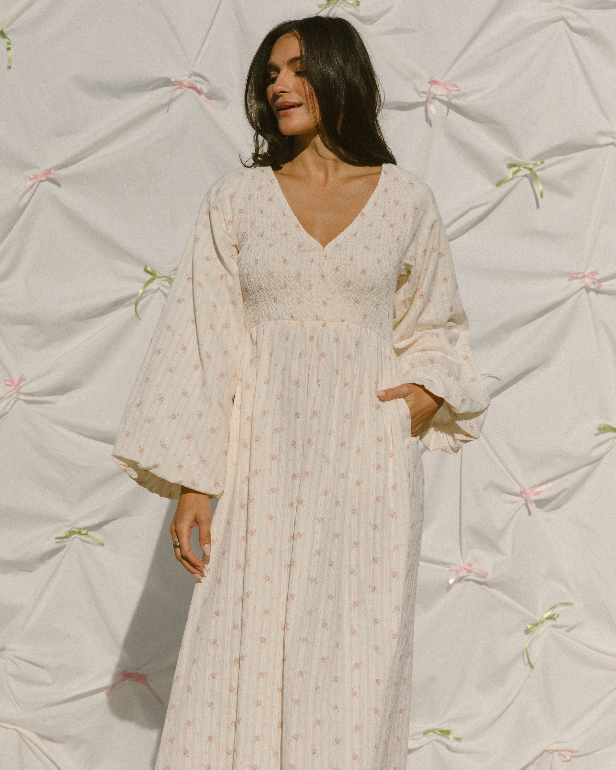 Woman wearing feminine long-sleeved dress with delicate cream and pink flower print. 