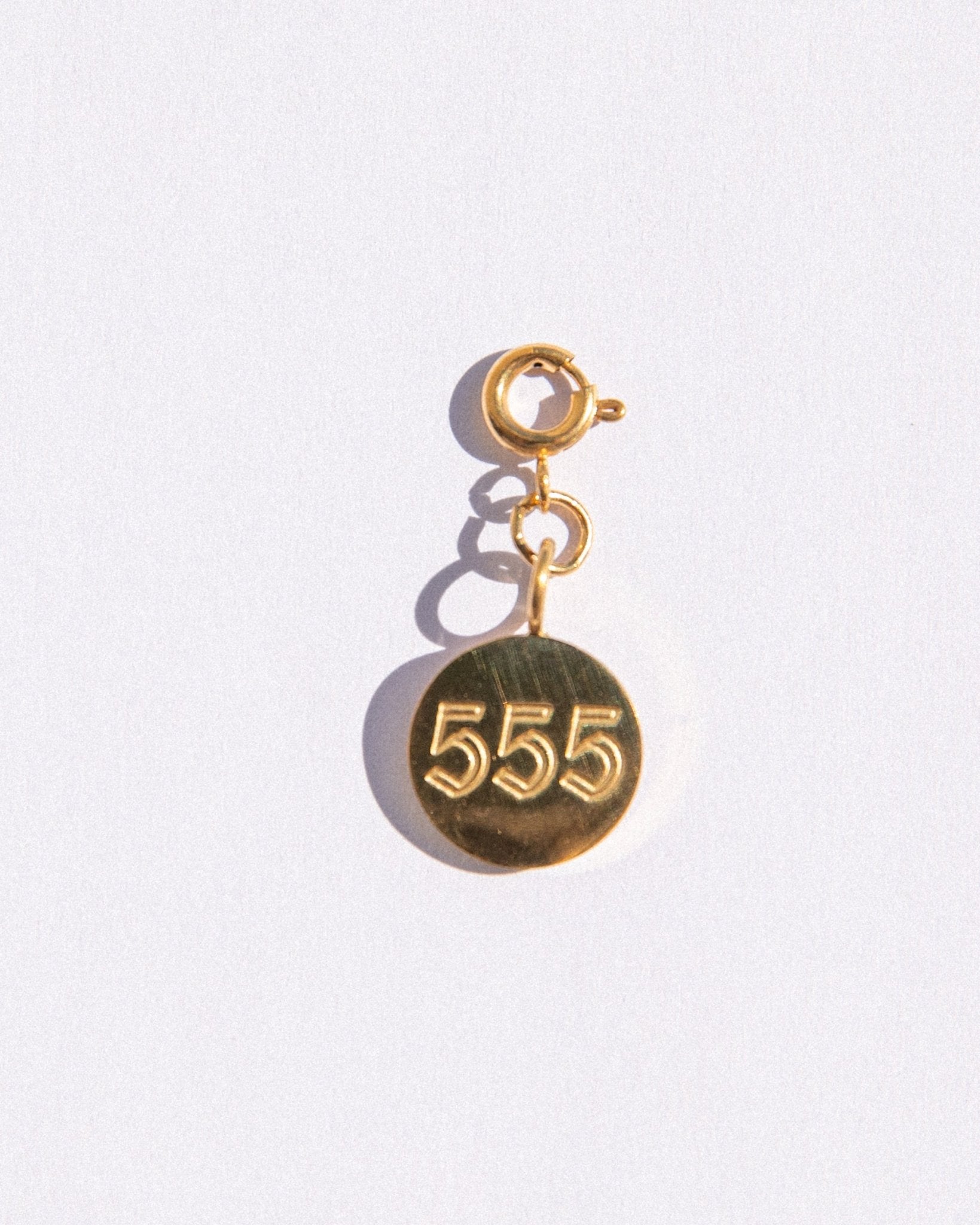 Gold circle charm with angel numbers '555' on a white background