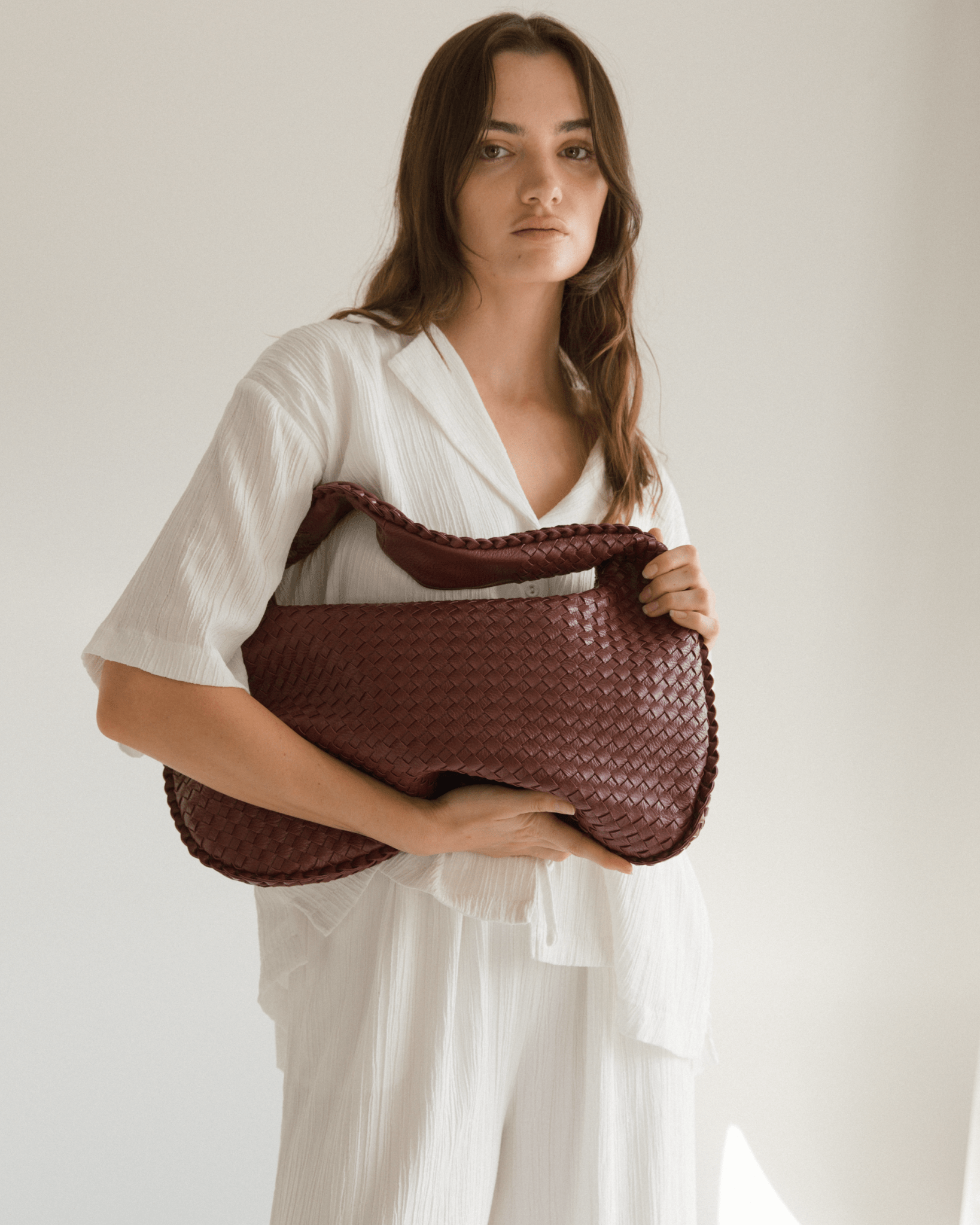 Woman holding a dark wine coloured bag against a plain background