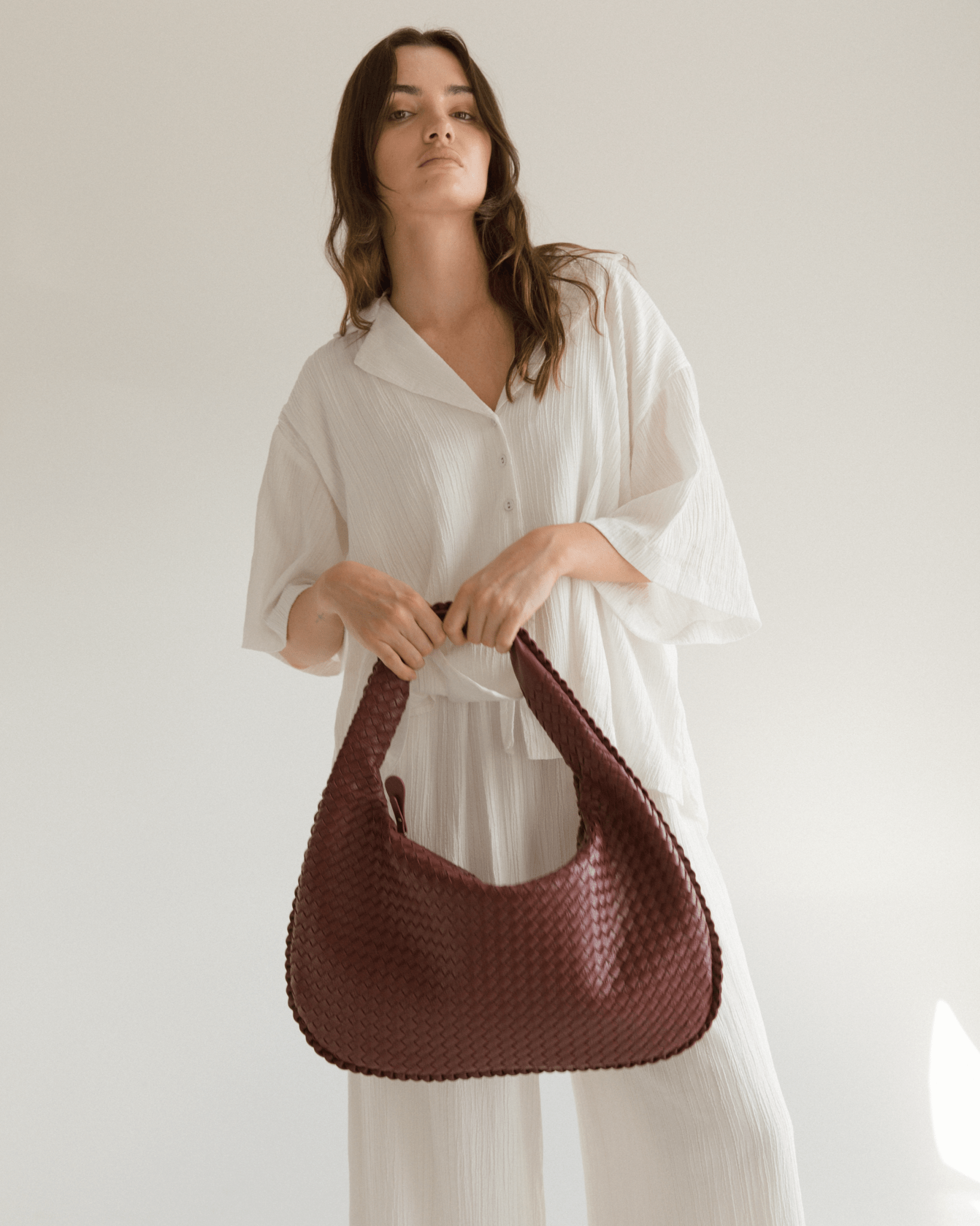 Woman holding a maroon woven handbag against a plain background