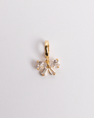 A gold-plated stainless steel and crystal bow charm with a secure clasp on a white background.