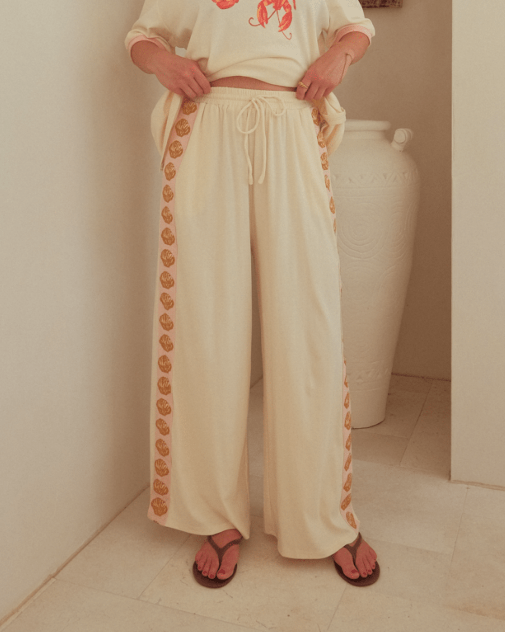 Woman wearing high-waisted beige wide-legged pants with drawstring waist. 