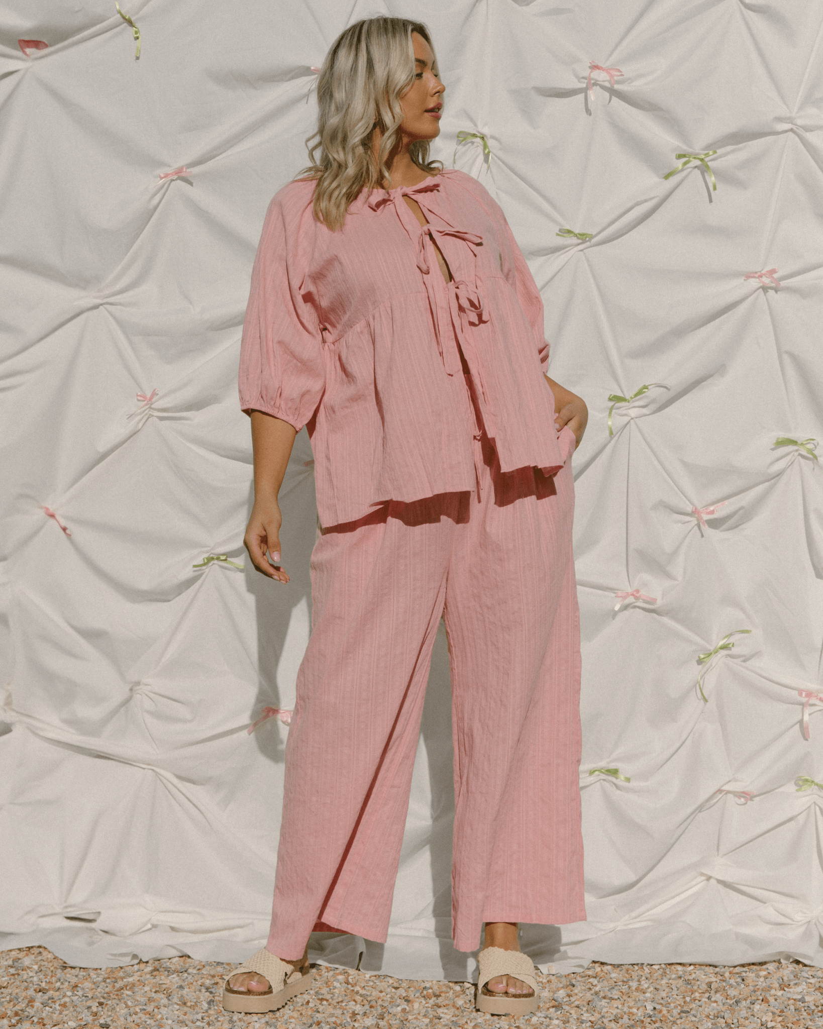 Woman wearing trendy pink shirt with bows down the front and matching pink wide-legged pants. 