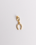 A gold-colored horseshoe-shaped charm with a clasp on one end, isolated on a white background.