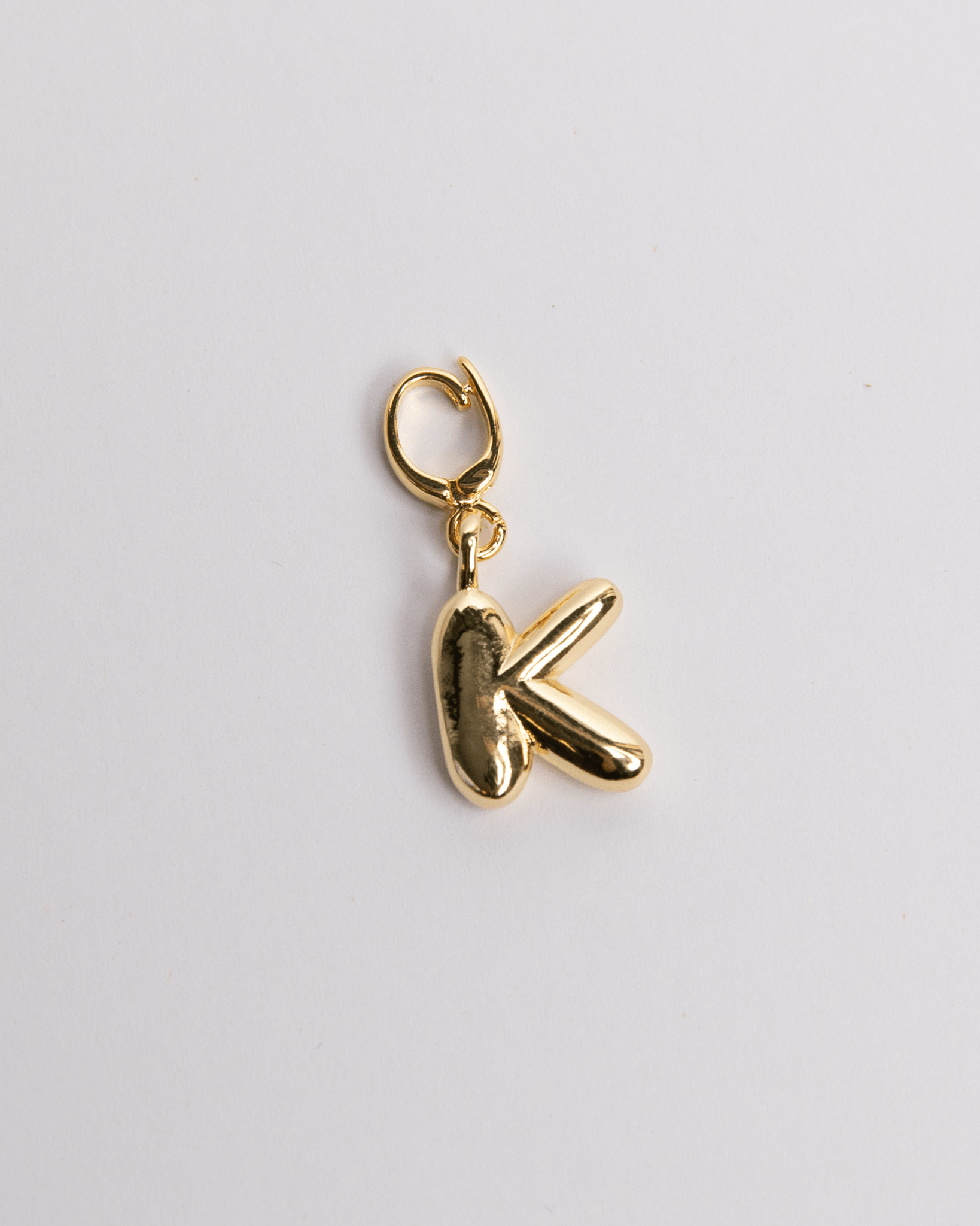 A gold-plated stainless steel charm in the shape of the letter K with a secure clasp designed for attaching to necklaces or bracelets.