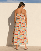 Woman wearing a colorful strapless dress against a white wall