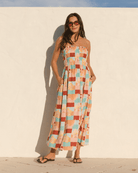 Woman wearing a colorful strapless dress against a white wall.