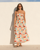 Woman wearing a colorful checkered dress against a white wall.