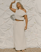 Woman in a light-colored outfit standing against a textured white wall with decorative bows.