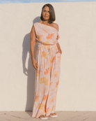 Woman wearing off the shoulder crop top and matching wide legged pants in a light pink floral design. 