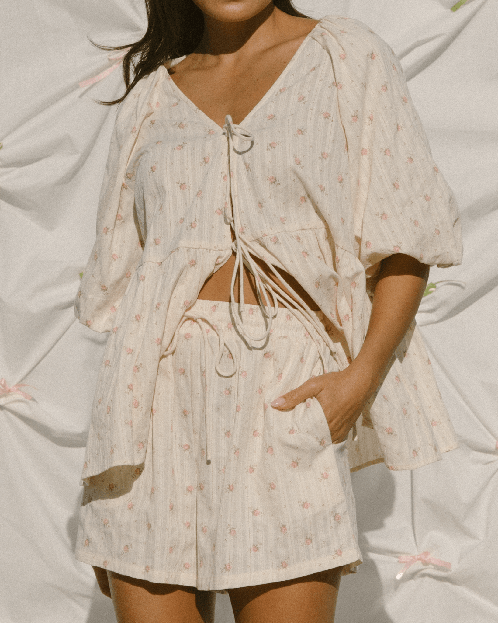 Woman wearing a delicate cream coloured shirt with pink flowers and matching shorts. 