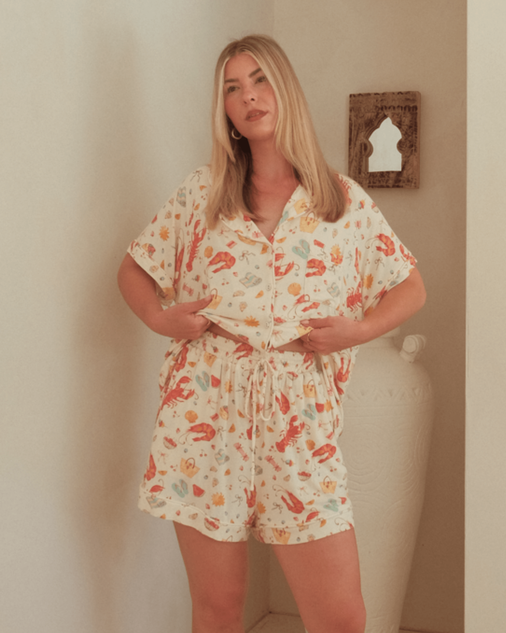 Woman wearing a pajama set standing against a plain wall.