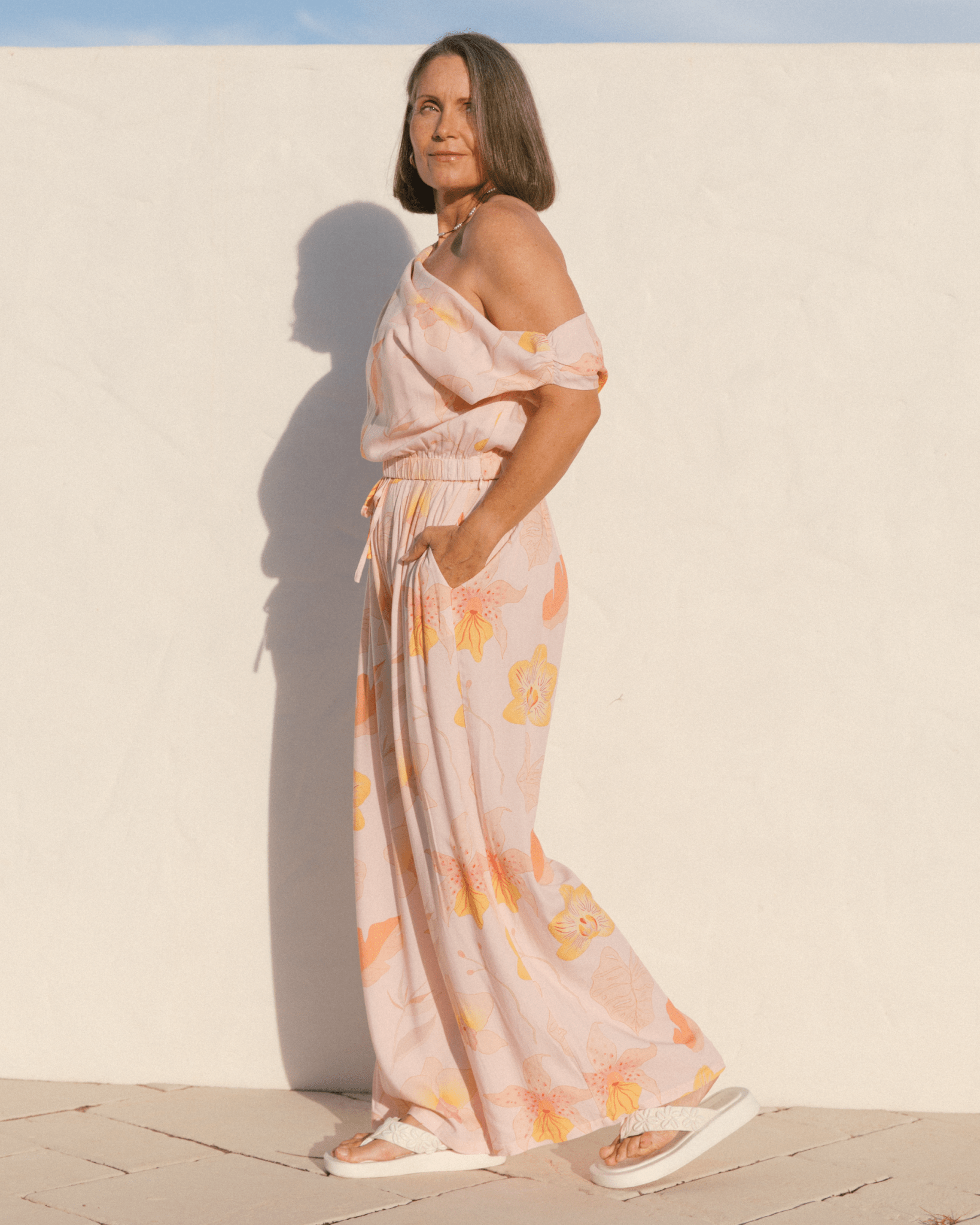 Woman wearing a floral set and standing against a white wall.