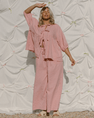 Woman wearing pink matching set with billowing sleeved tie-up top with breastfeeding access. 