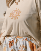 Beige oversized, wide tee with watercolour style sun graphic print & blue high waisted pants with summer pawpaw and pineapple floral print. 