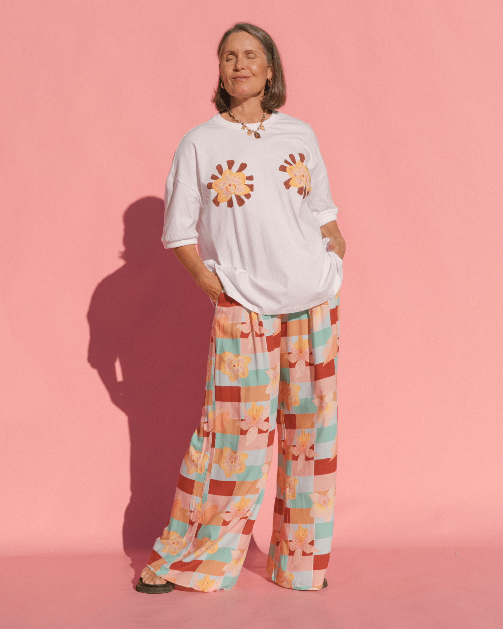 Model wearing white oversized slouch tee with floral graphic paired with blue and red geometric floral print pants. 
